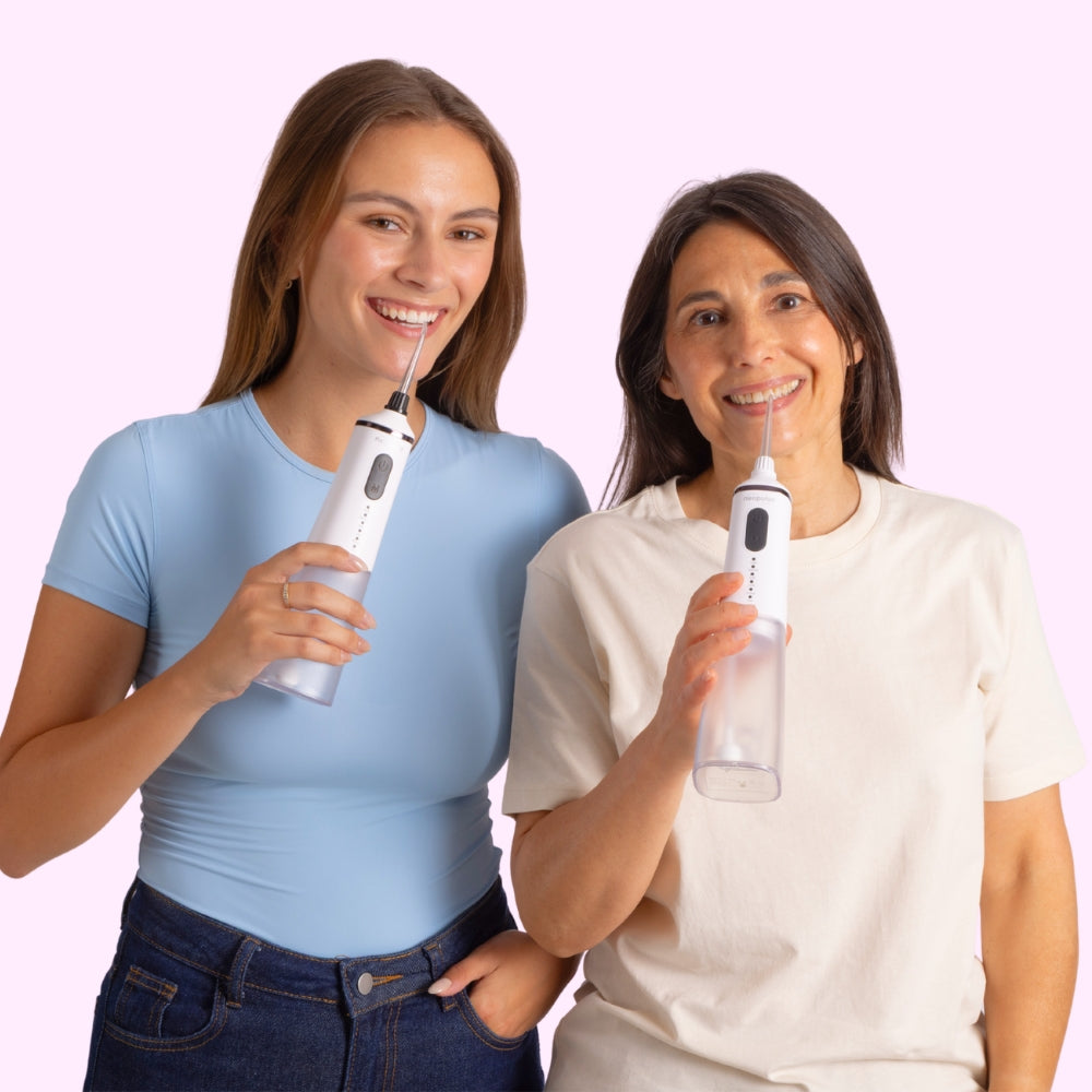 Deux femmes souriantes utilisant le jet dentaire EASY sur fond rose 